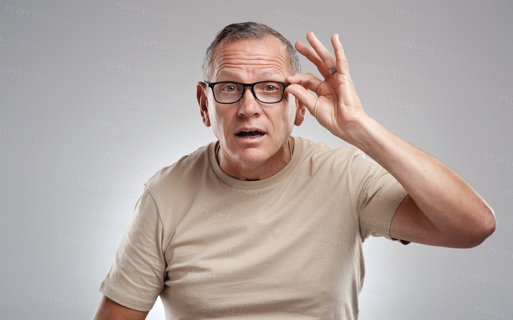 Buy stock photo Shot of a handsome mature man standing alone against a grey background in the studio and adjusting his glasses