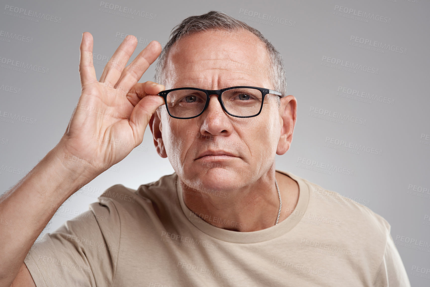 Buy stock photo Shot of a handsome mature man standing alone against a grey background in the studio and adjusting his glasses