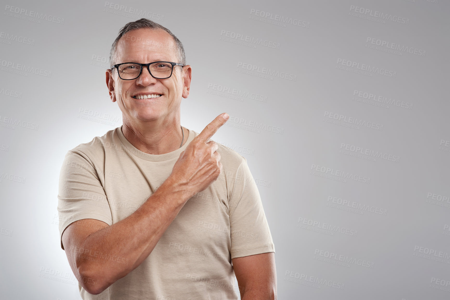 Buy stock photo Shot of a handsome mature man standing alone against a grey background in the studio and pointing at a promotion