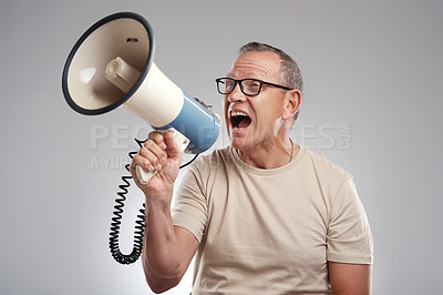 Buy stock photo Shot of a handsome mature man standing alone against a grey background in the studio and using a megaphone