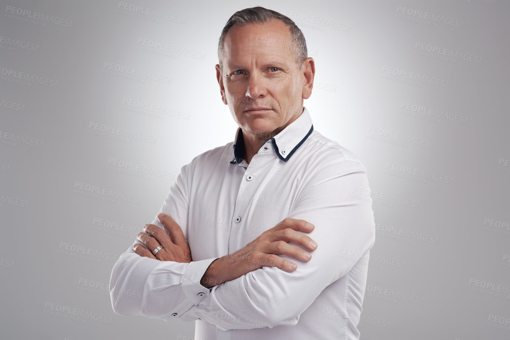 Buy stock photo Shot of a handsome mature businessman standing alone against a grey background in the studio with his arms folded