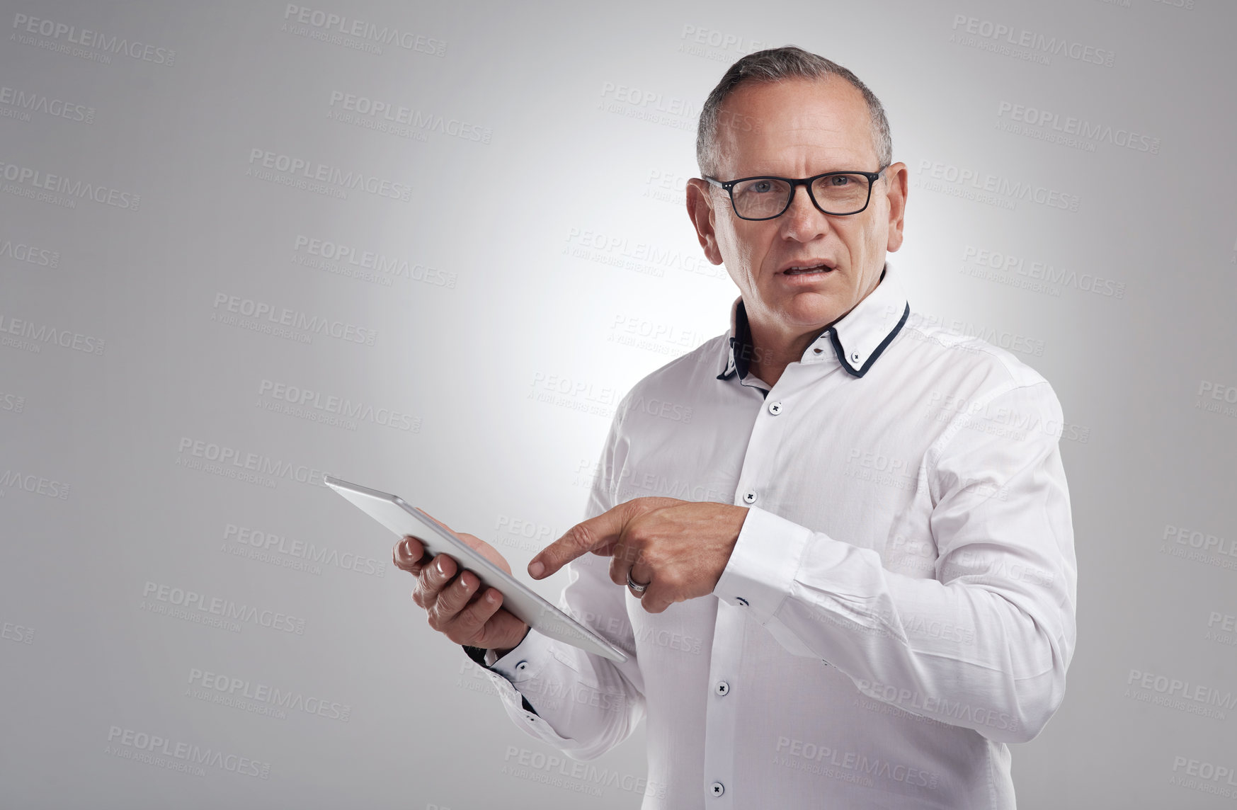 Buy stock photo Shot of a handsome mature businessman standing alone against a grey background in the studio and using a digital tablet