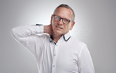 Buy stock photo Shot of a handsome mature businessman standing alone against a grey background in the studio and suffering from neck ache