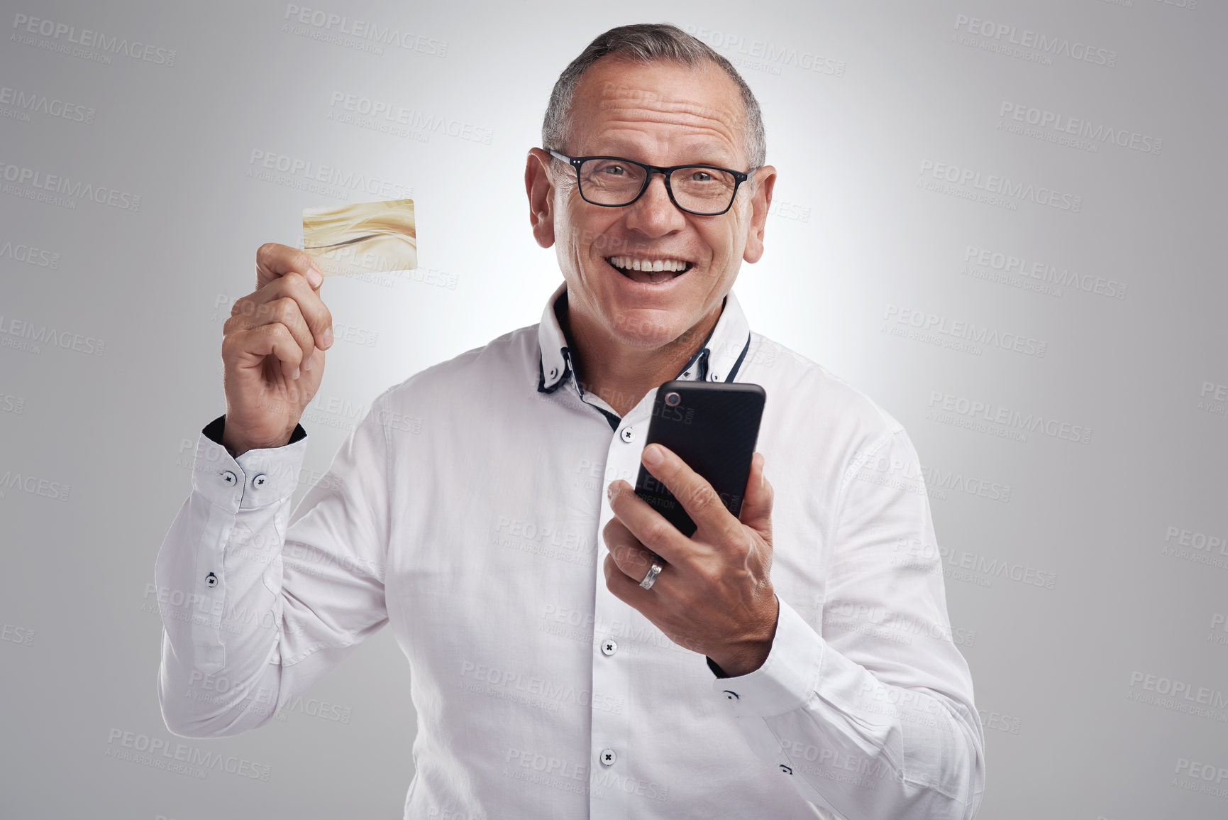 Buy stock photo Shot of a handsome mature businessman standing against a grey studio background and using his cellphone for online shopping