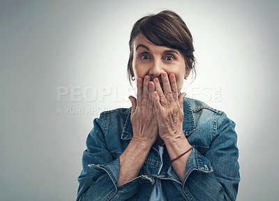Buy stock photo Studio portrait of a senior woman covering her mouth and looking shocked against a grey background