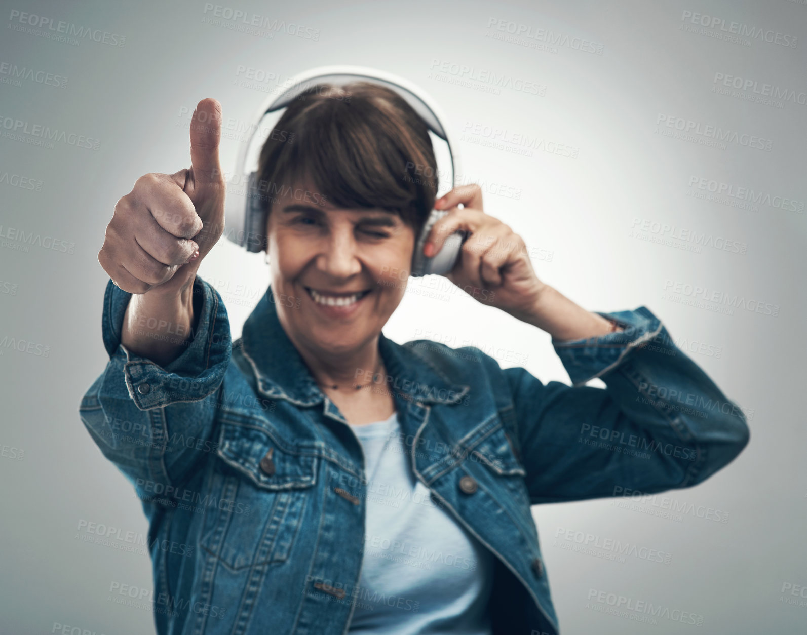 Buy stock photo Studio portrait of a senior woman showing thumbs up while wearing headphones against a grey background