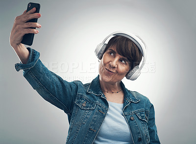 Buy stock photo Studio shot of a senior woman taking selfies while wearing headphones against a grey background