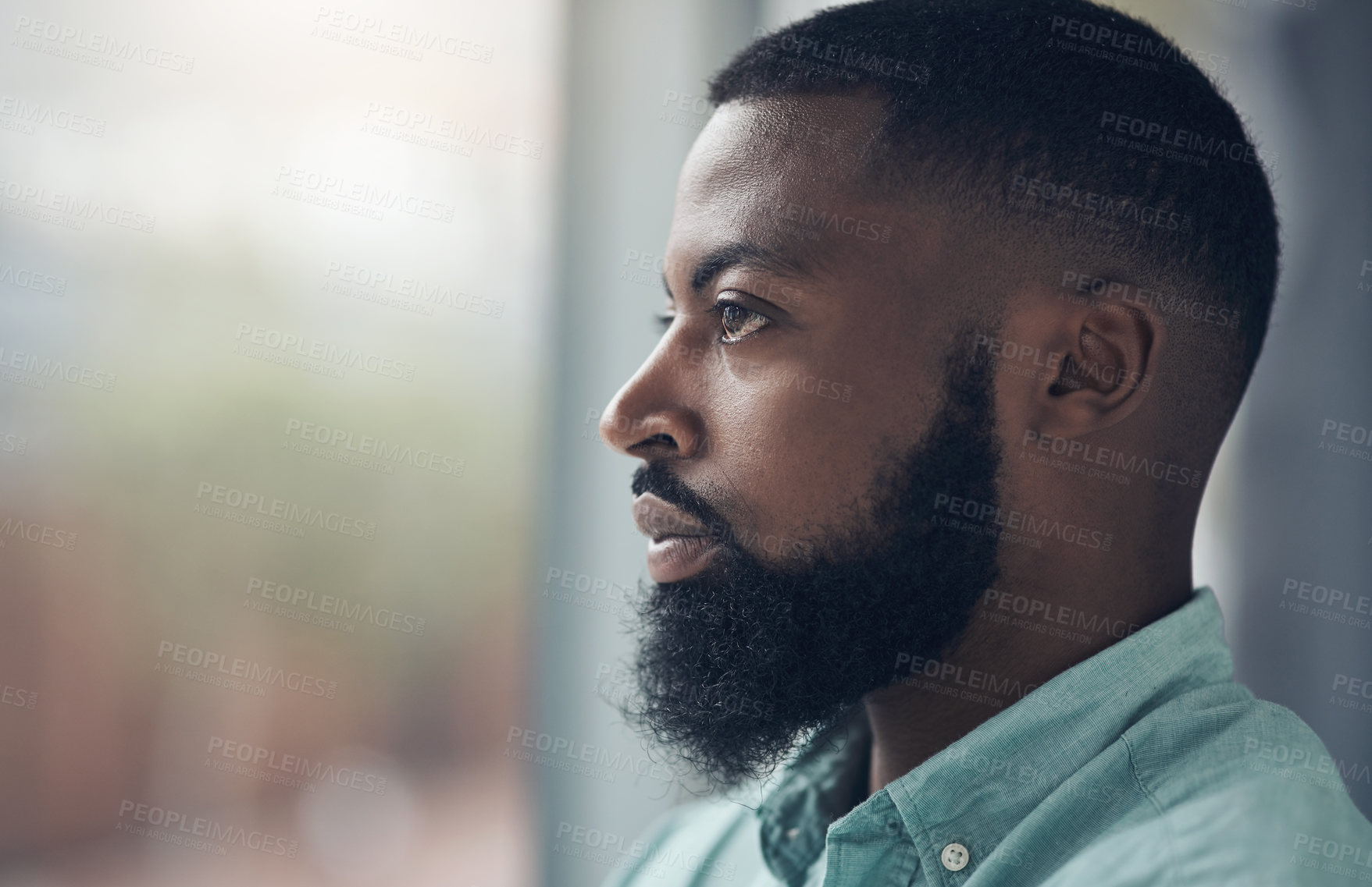 Buy stock photo Shot of a handsome young businessman standing alone in his office and looking outside his window contemplatively