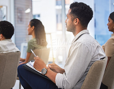 Buy stock photo Shot of a young man taking notes during a meeting at work in a modern office