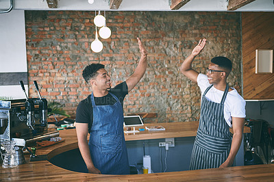 Buy stock photo Shot of two confident young men giving each other a high five while working in a cafe