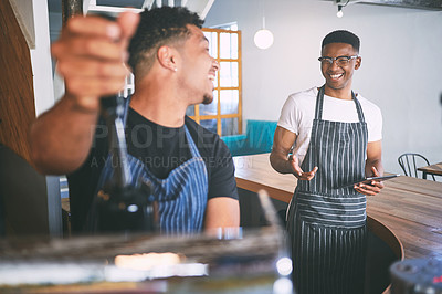 Buy stock photo Shot of two young men using a digital tablet while making coffee at a cafe