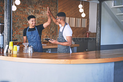 Buy stock photo Shot of two confident young men using a digital tablet and giving each other a high five while working in a cafe