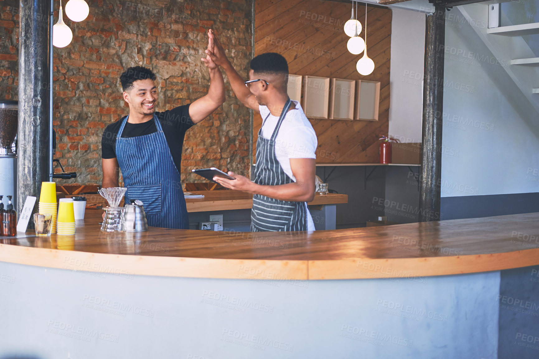 Buy stock photo Shot of two confident young men using a digital tablet and giving each other a high five while working in a cafe