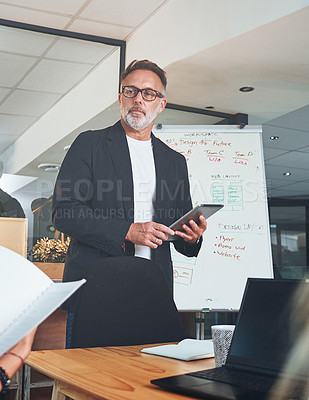 Buy stock photo Shot of a mature businessman using a digital tablet while delivering a presentation in the boardroom of a modern office