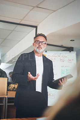 Buy stock photo Shot of a mature businessman using a digital tablet while delivering a presentation in the boardroom of a modern office