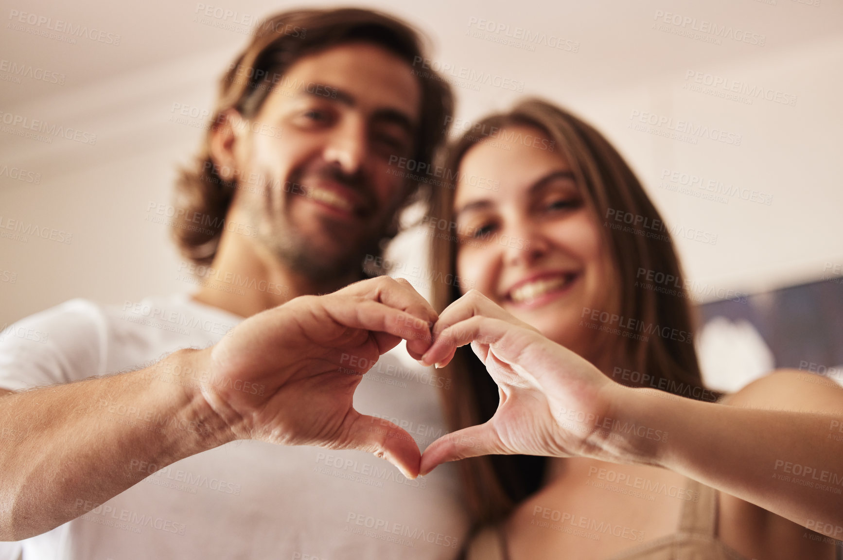 Buy stock photo Shot of a young couple making a heart sign with their hands at home