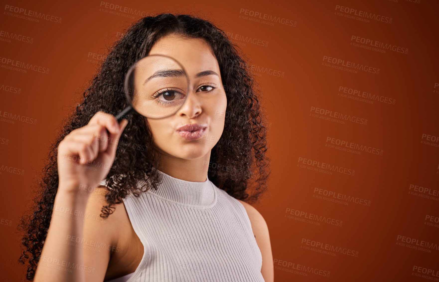 Buy stock photo Cropped portrait of an attractive young woman looking through a magnifying glass in studio against a red background