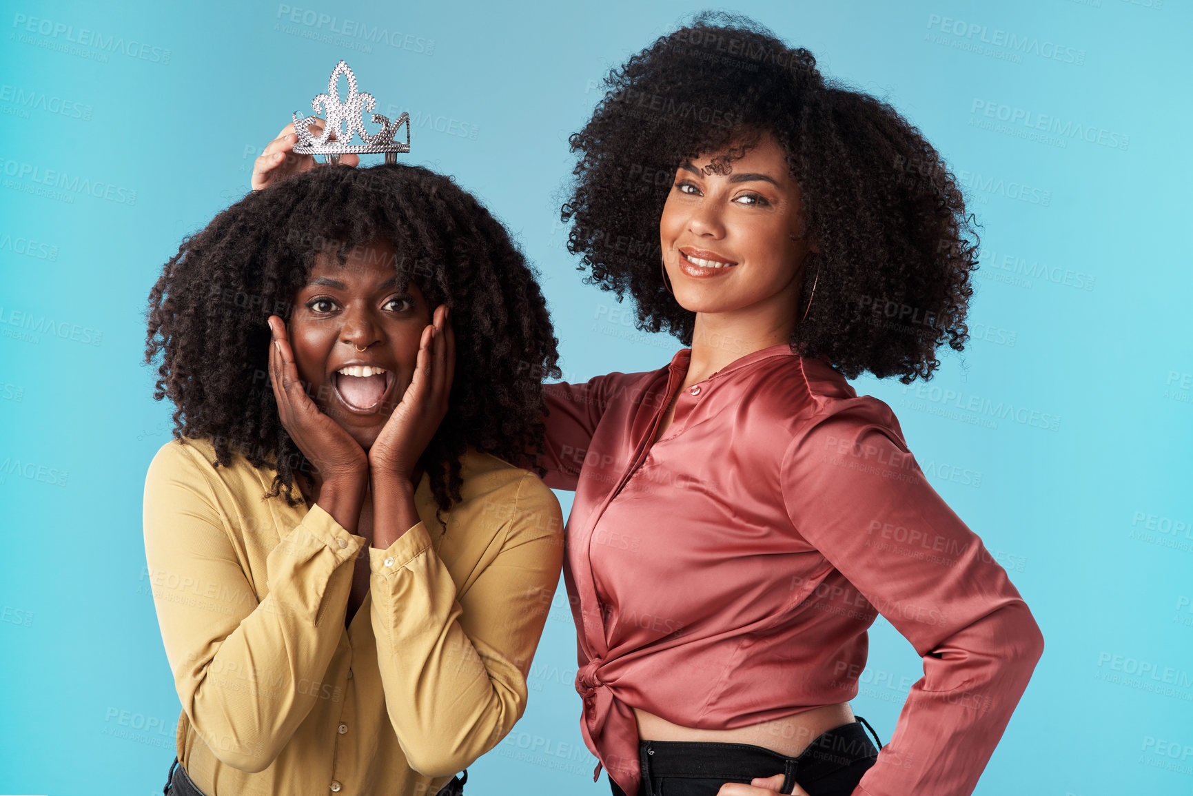 Buy stock photo Studio shot of a young woman putting a crown on her friend against a blue background