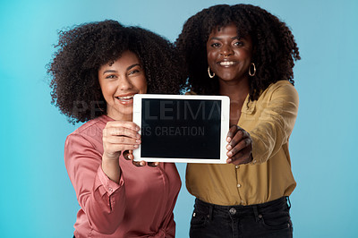 Buy stock photo Studio shot of two young women holding a digital tablet with a blank screen against a blue background