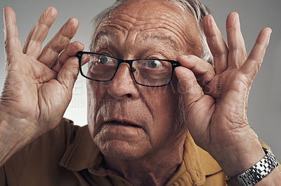 Buy stock photo Studio shot of an elderly man adjusting his spectacles against a grey background