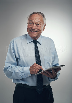 Buy stock photo Shot of a senior businessman standing alone against a grey background in the studio and using a digital tablet