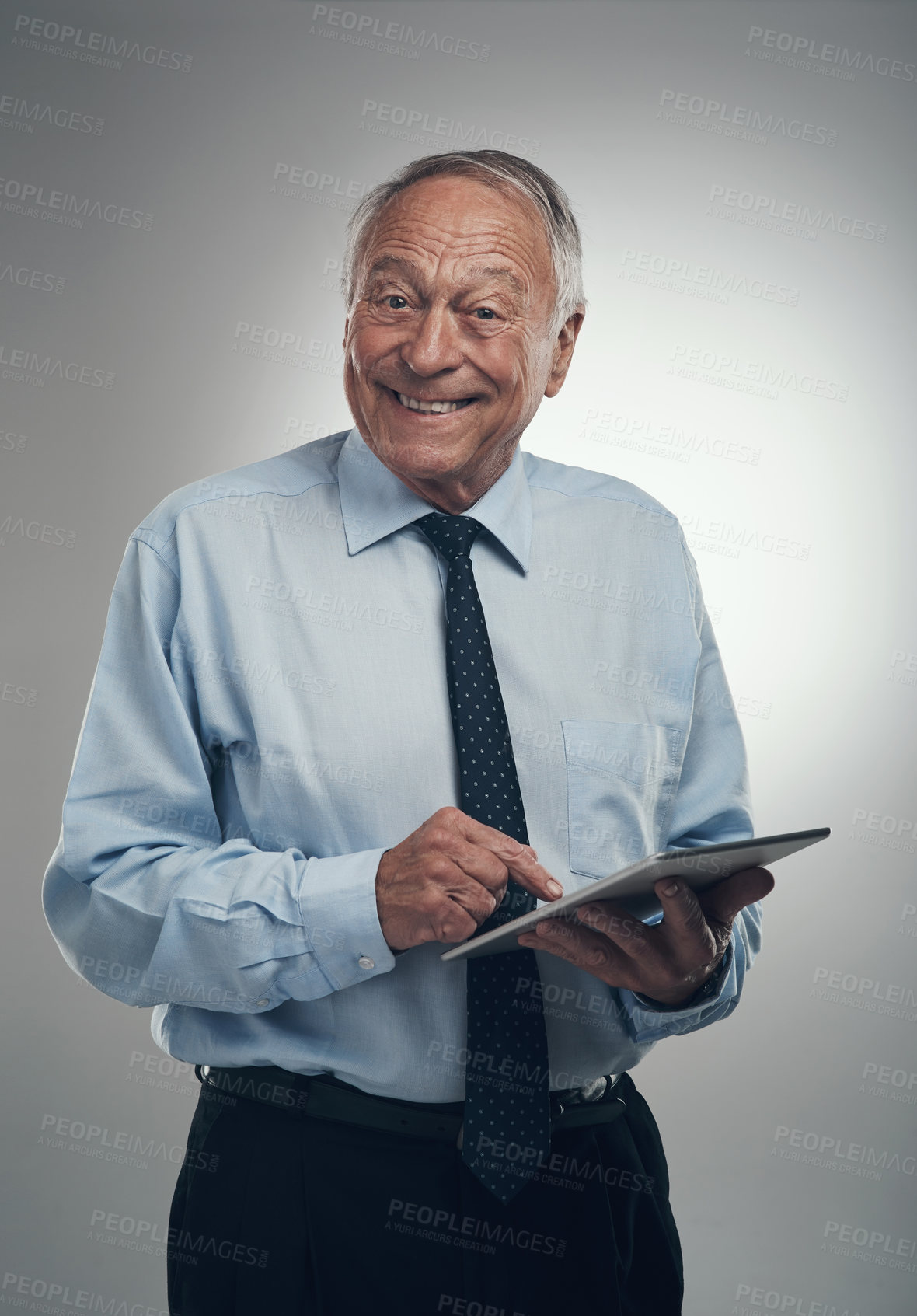 Buy stock photo Shot of a senior businessman standing alone against a grey background in the studio and using a digital tablet