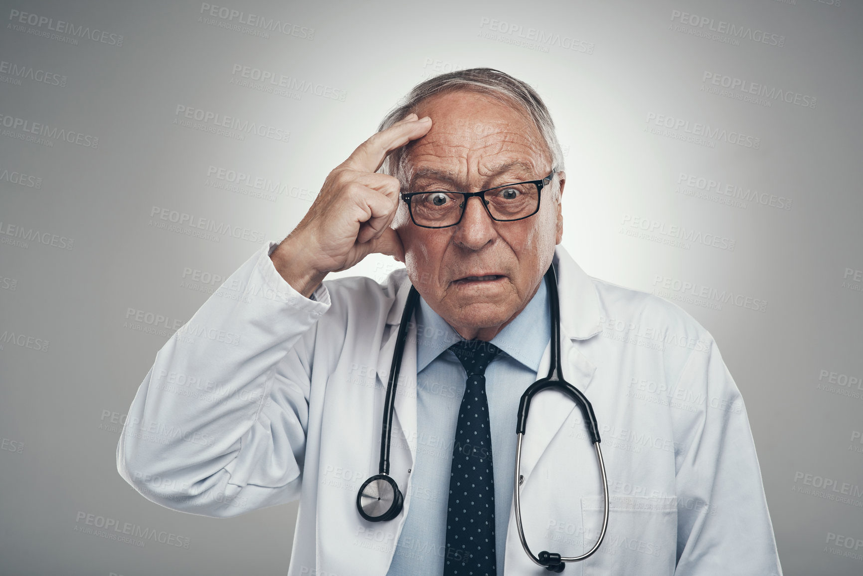 Buy stock photo Shot of an elderly male doctor grasping his head in a studio against a grey background
