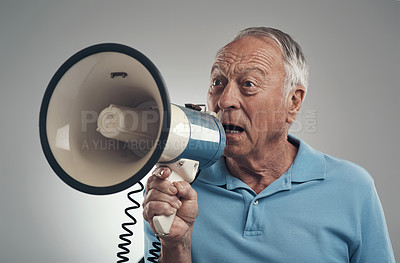 Buy stock photo Shot of an old man holding and speaking through a loud hailer in a studio against a grey background