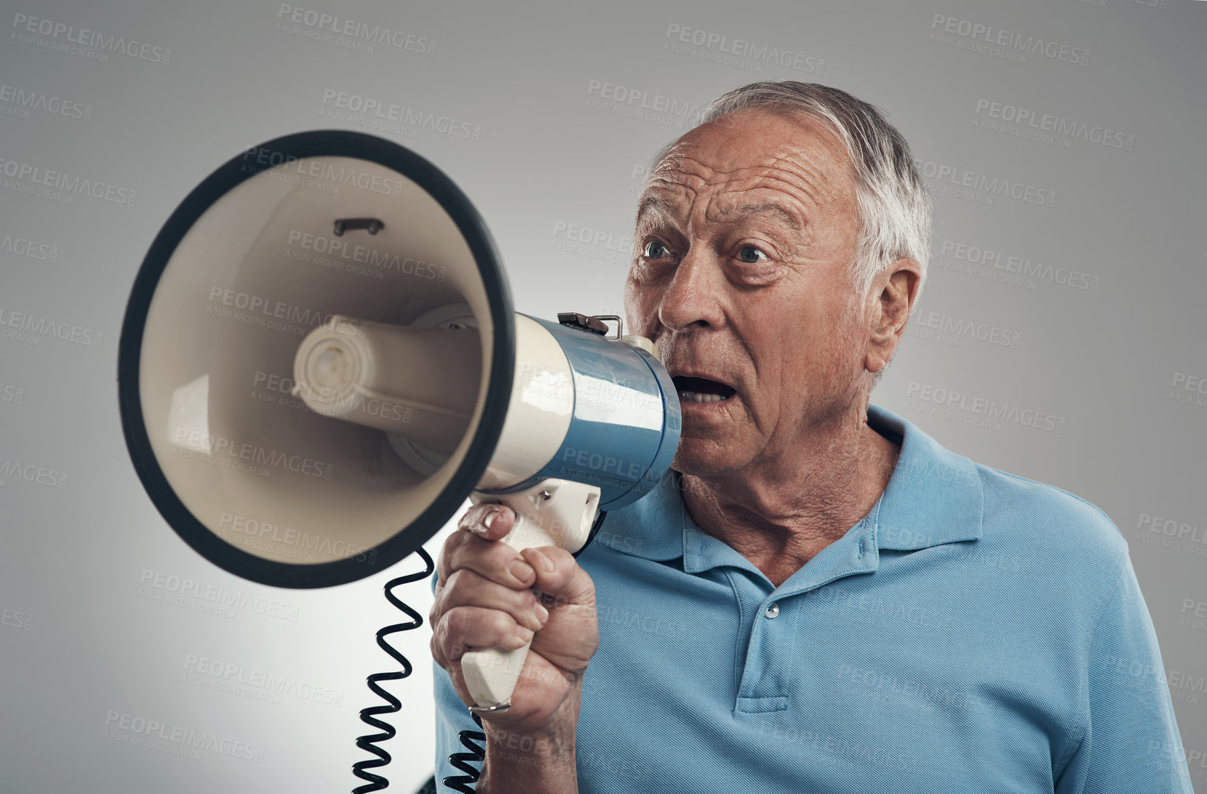 Buy stock photo Shot of an old man holding and speaking through a loud hailer in a studio against a grey background