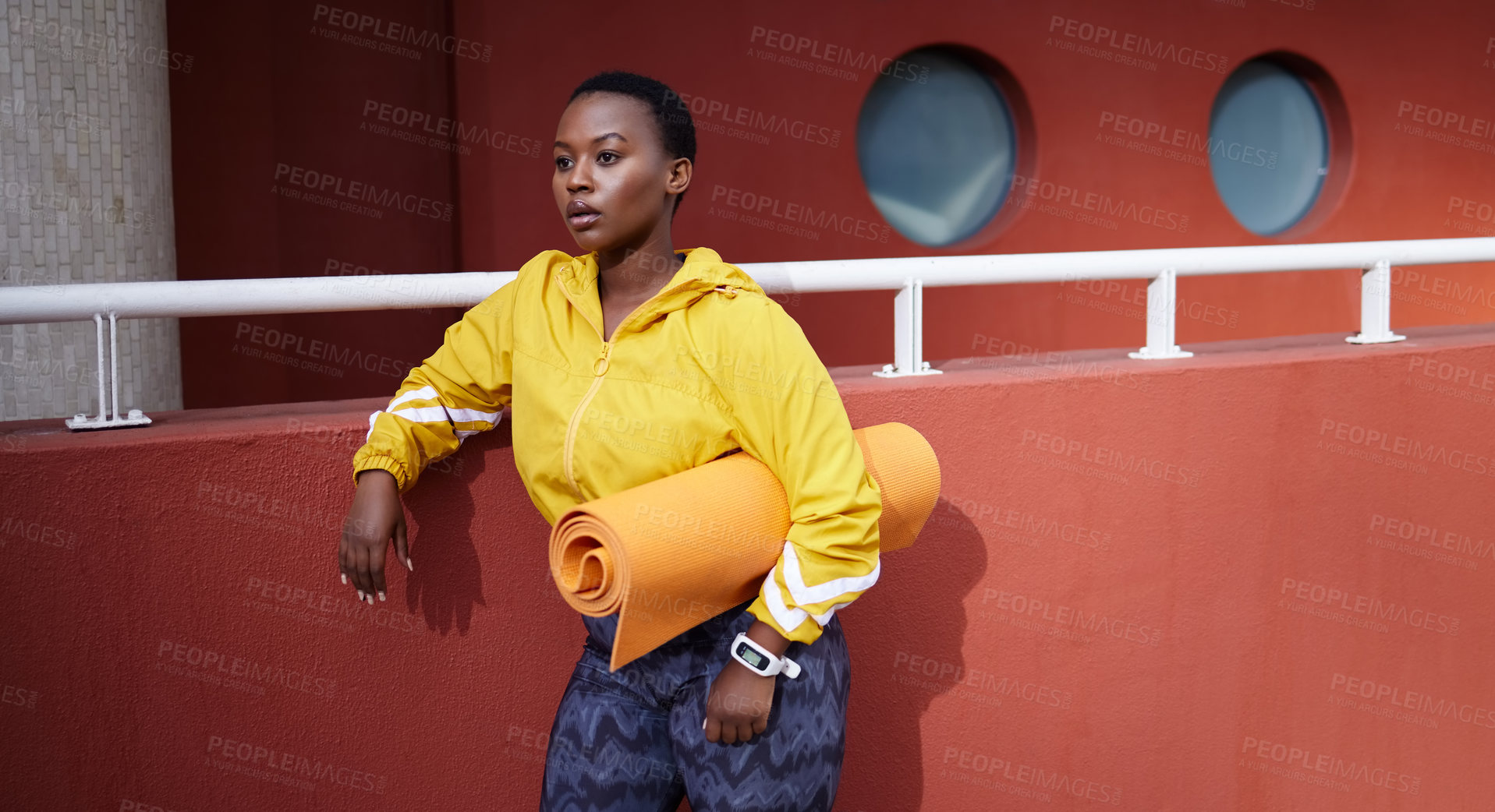 Buy stock photo Shot of a young woman holding an exercise mat looking thoughtful against an urban background