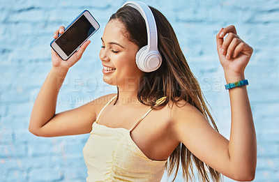 Buy stock photo Cropped shot of an attractive young woman wearing headphones and dancing outside against a blue background