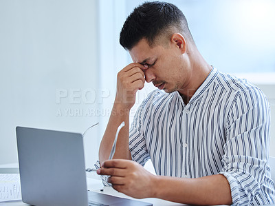 Buy stock photo Shot of a young businessman sitting alone in the office and suffering from a headache