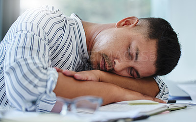 Buy stock photo Shot of a young businessman feeling exhausted and sleeping on his desk in his office