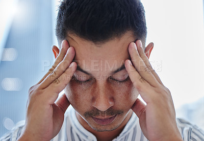 Buy stock photo Shot of a young businessman sitting alone in the office and suffering from a headache