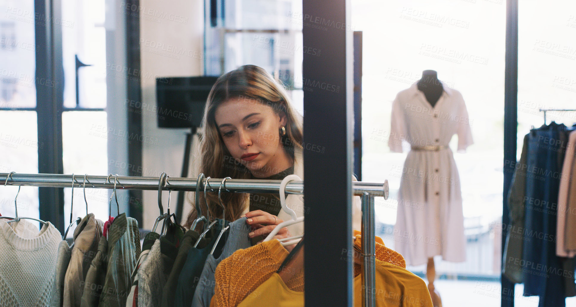 Buy stock photo Shot of a young woman browsing through clothes in a boutique