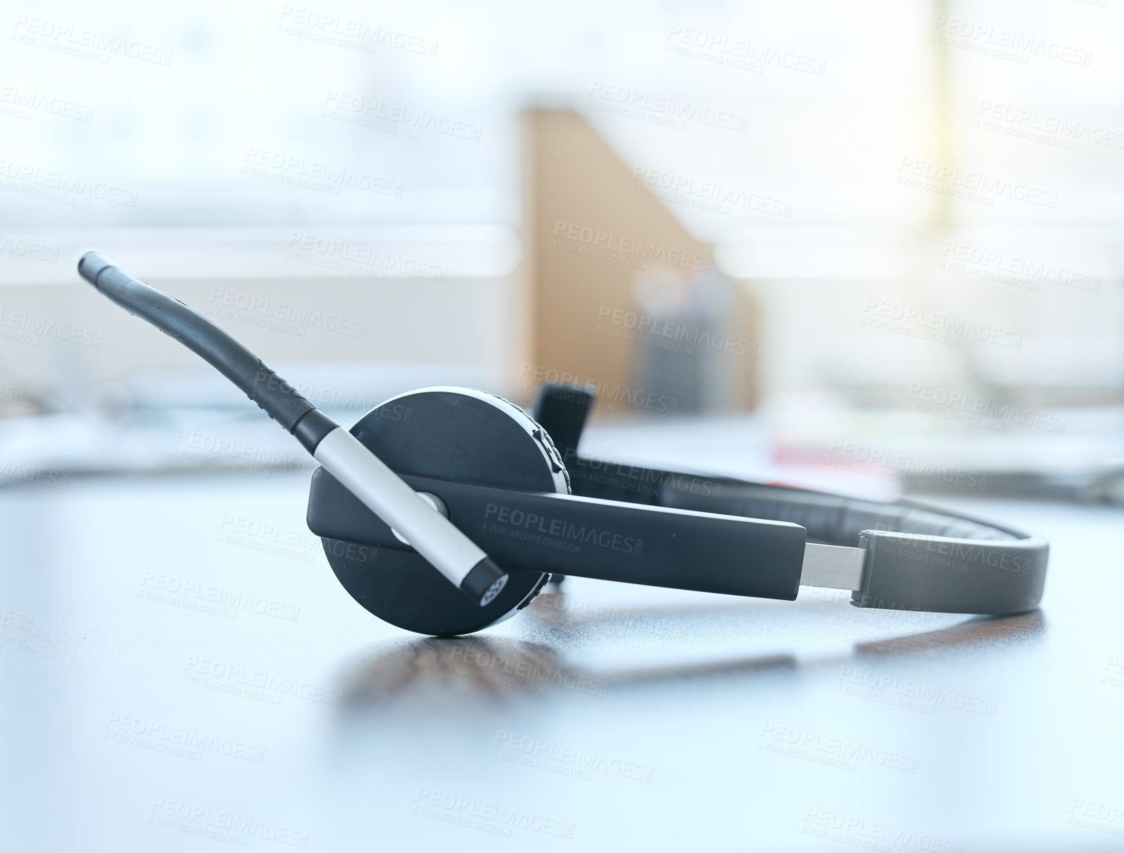 Buy stock photo Shot of a set of headsets lying on a desk in an empty office during the day