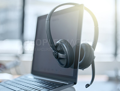 Buy stock photo Shot of a set of headsets resting on a laptop in an empty office during the day
