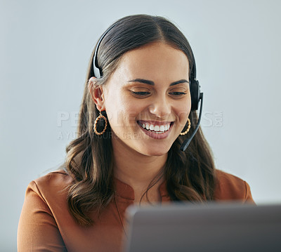 Buy stock photo Shot of an attractive young saleswoman sitting alone in her office and wearing a headset while using her laptop