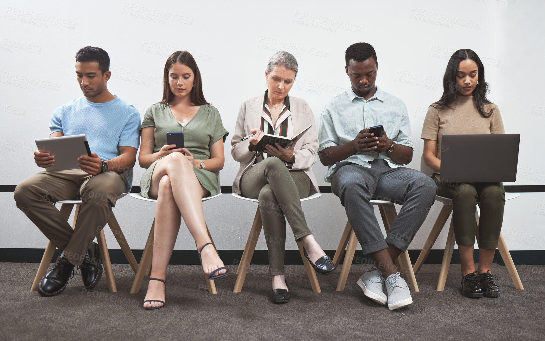 Buy stock photo Shot of a group of businesspeople using digital devices while sitting together in a line against a white wall