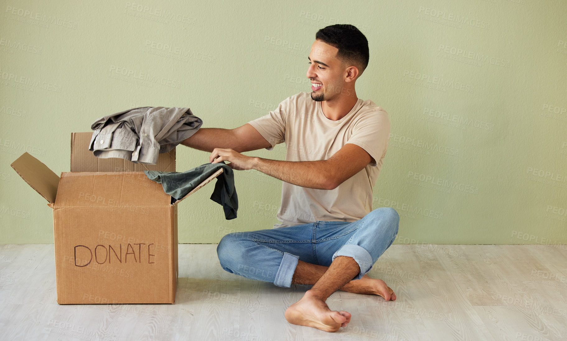 Buy stock photo Shot of a young man putting clothes into a donation box at home