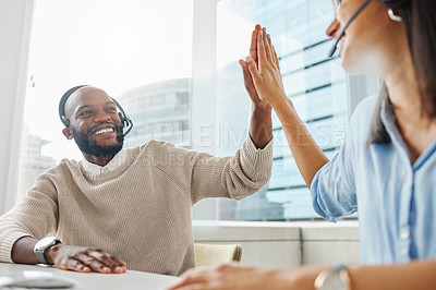 Buy stock photo Shot of two young call centre agents sitting together in the office and giving each other a high five