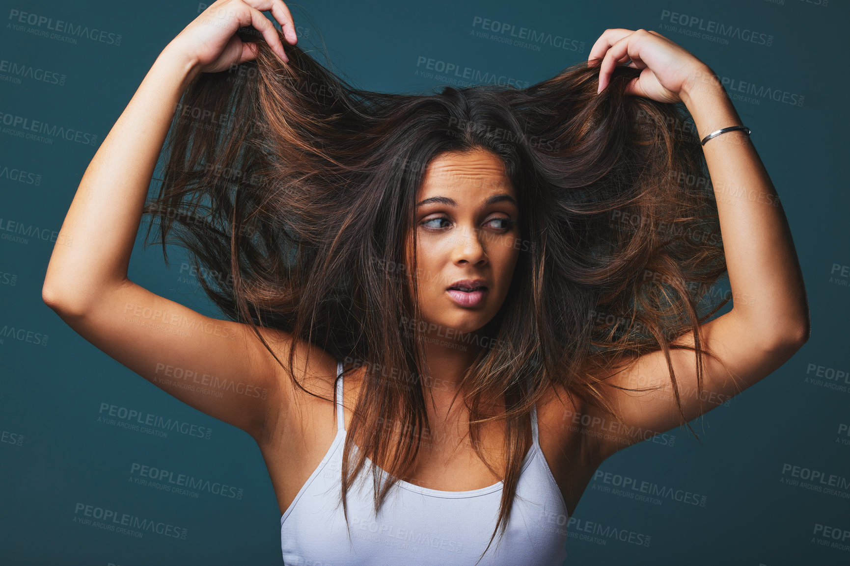 Buy stock photo Studio shot of a beautiful young woman pulling on her hair posing against a blue background