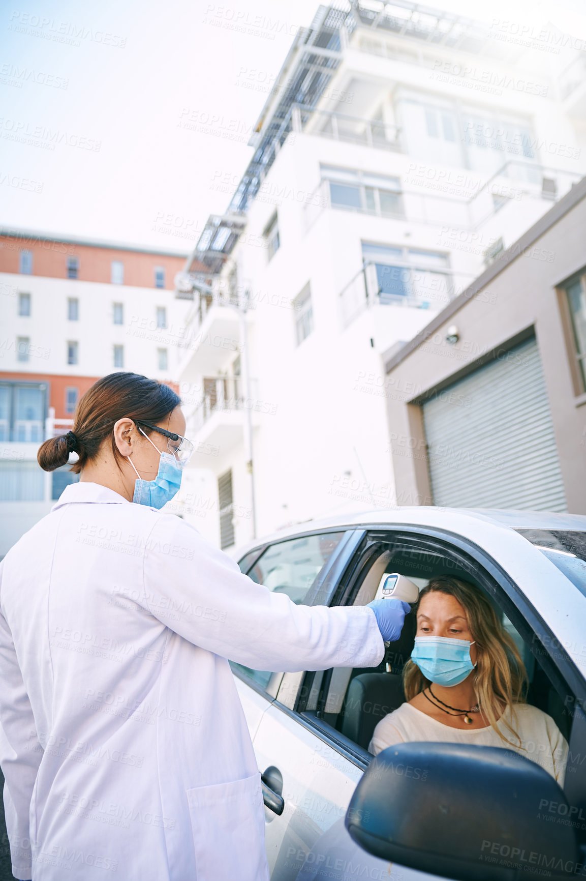 Buy stock photo Shot of a masked young woman getting her temperature checked by a doctor while sitting in her car