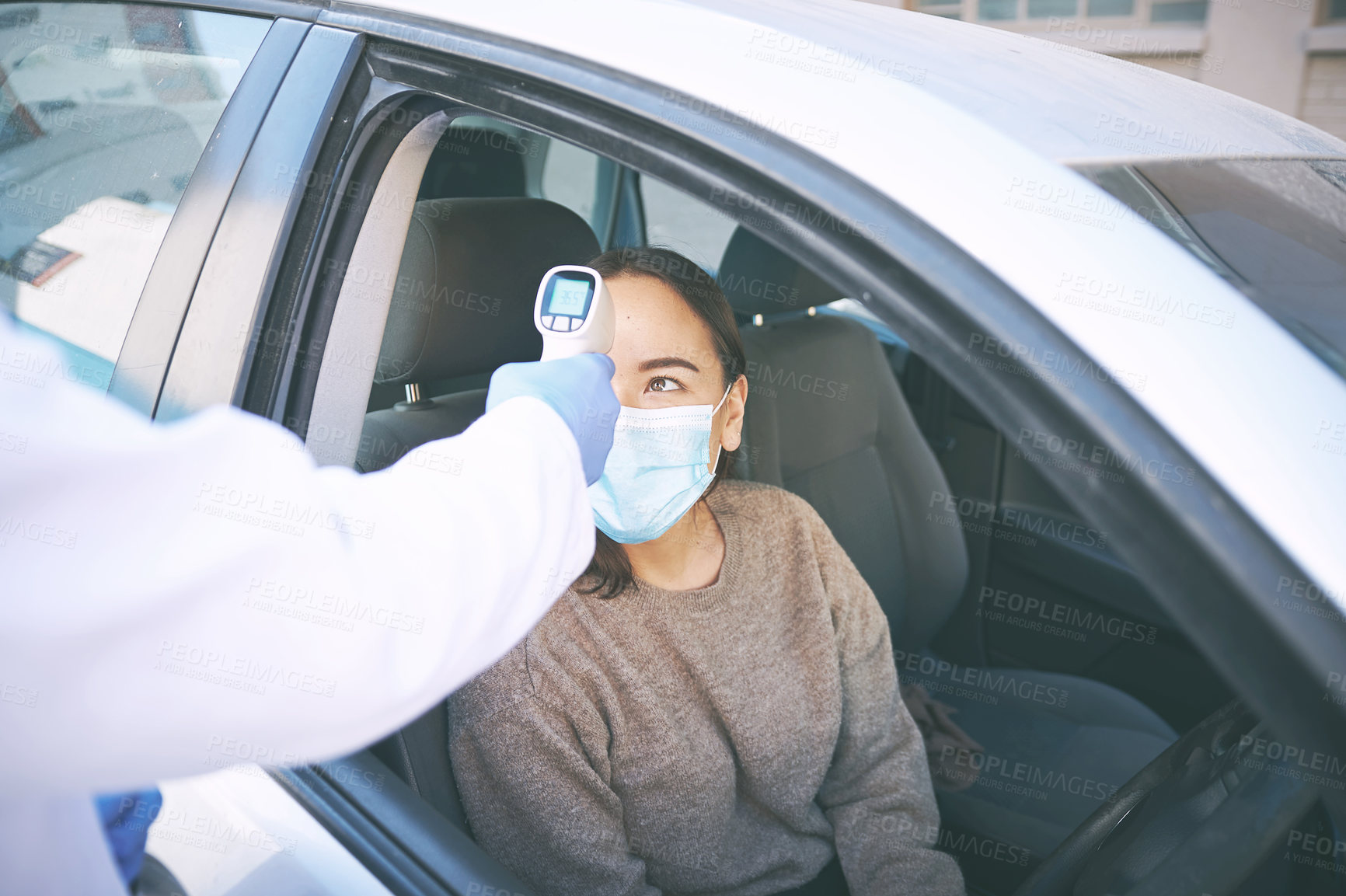 Buy stock photo Shot of a masked young woman getting her temperature checked by a doctor while sitting in her car