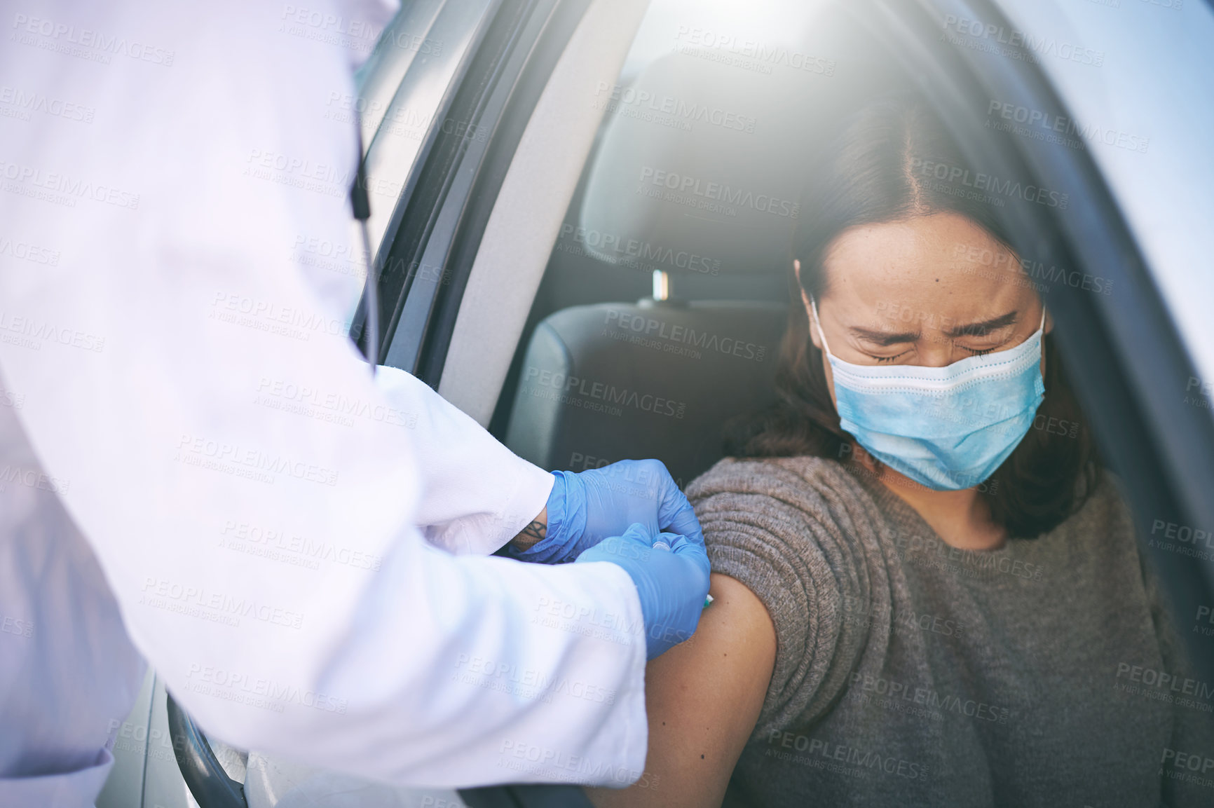 Buy stock photo Shot of a masked young woman receiving an injection at a Covid-19 drive through testing centre