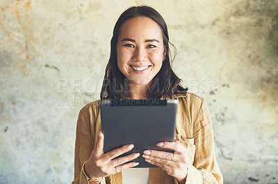 Buy stock photo Portrait of a young woman using a digital tablet while standing against a wall