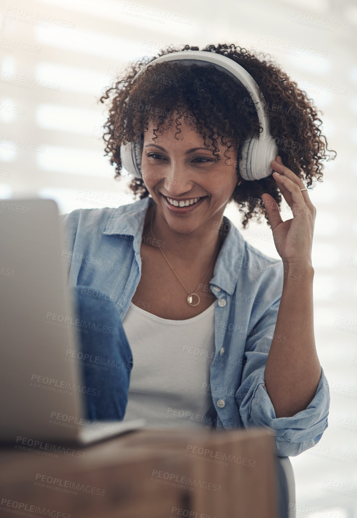 Buy stock photo Shot of an attractive young woman sitting alone at home and using her laptop while wearing headphones