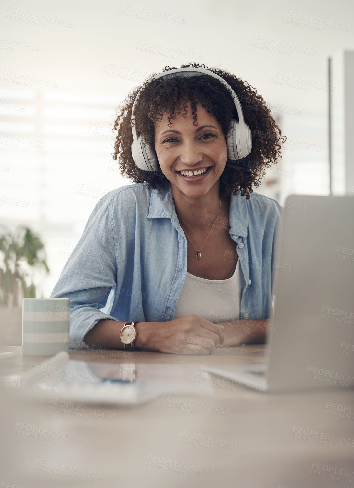 Buy stock photo Shot of an attractive young woman sitting alone at home and using her laptop while wearing headphones