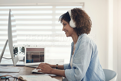 Buy stock photo Shot of an attractive young woman sitting alone at home and using her computer while wearing headphones