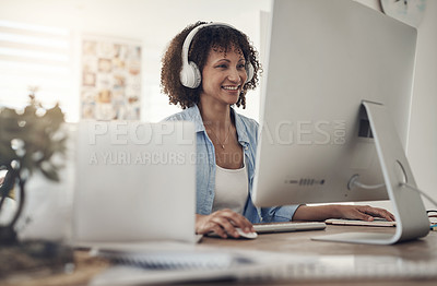 Buy stock photo Shot of an attractive young woman sitting alone at home and using her computer while wearing headphones